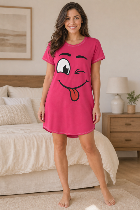 A woman stands in a bedroom wearing a bright pink short-sleeve nightgown with a large cartoon face graphic on the front. The graphic shows one winking eye and a sticking-out tongue.